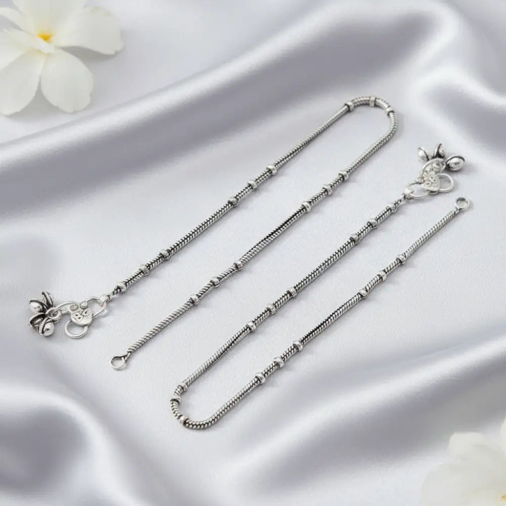 Silver anklets on a satin surface with a white flower