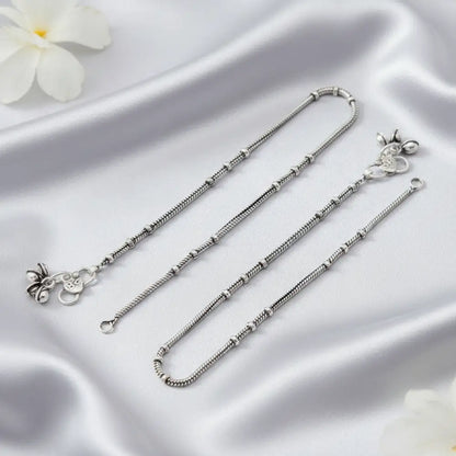 Silver anklets on a satin surface with a white flower