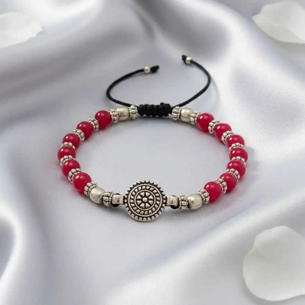 Bracelet with red beads and silver circular charm on a white fabric background
