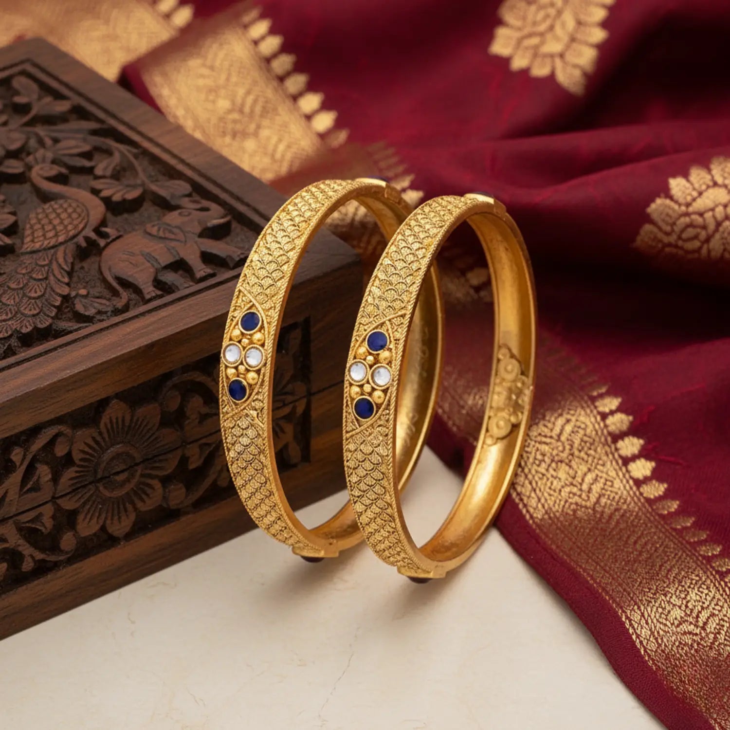 Gold bangles with blue and white stones on a red fabric background