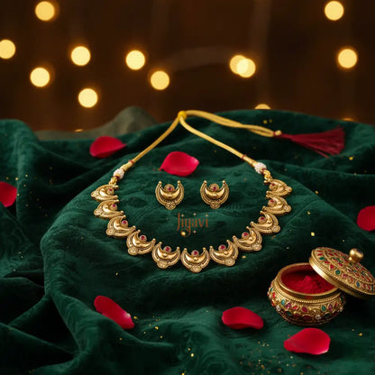 Gold necklace and earrings set on a green fabric with red petals and a blurred light background