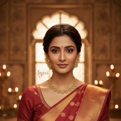 Woman wearing gold jewelry and a red saree with a warm, blurred background