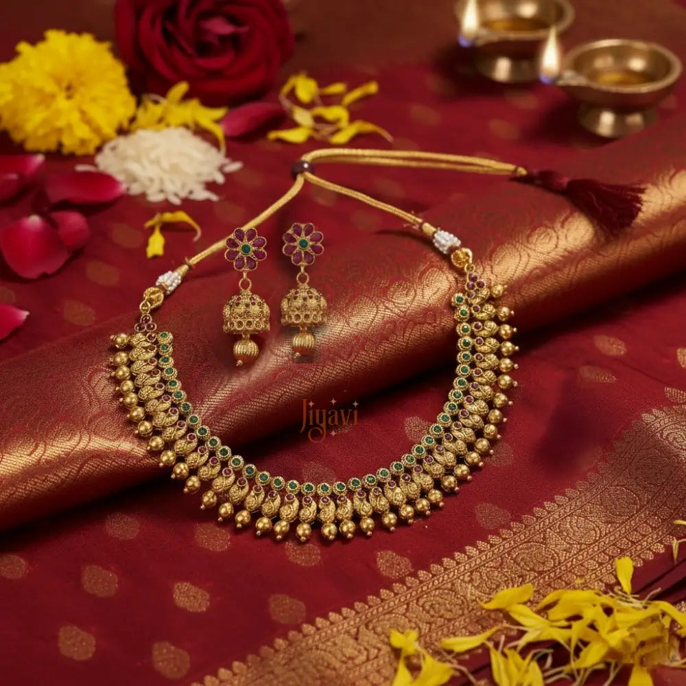 Gold necklace and earrings on a red fabric background with flowers and Diwali lamps.