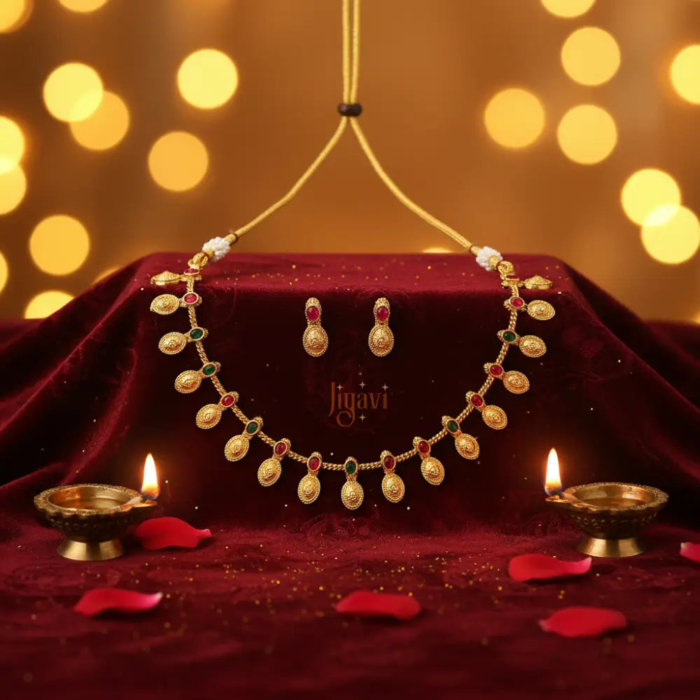 Gold necklace and earrings on a red fabric with 'Jiyavi' branding, set against a warm bokeh background.