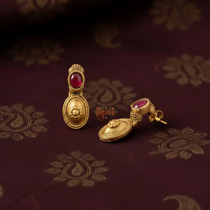 Gold earrings with red gemstones on a patterned fabric background