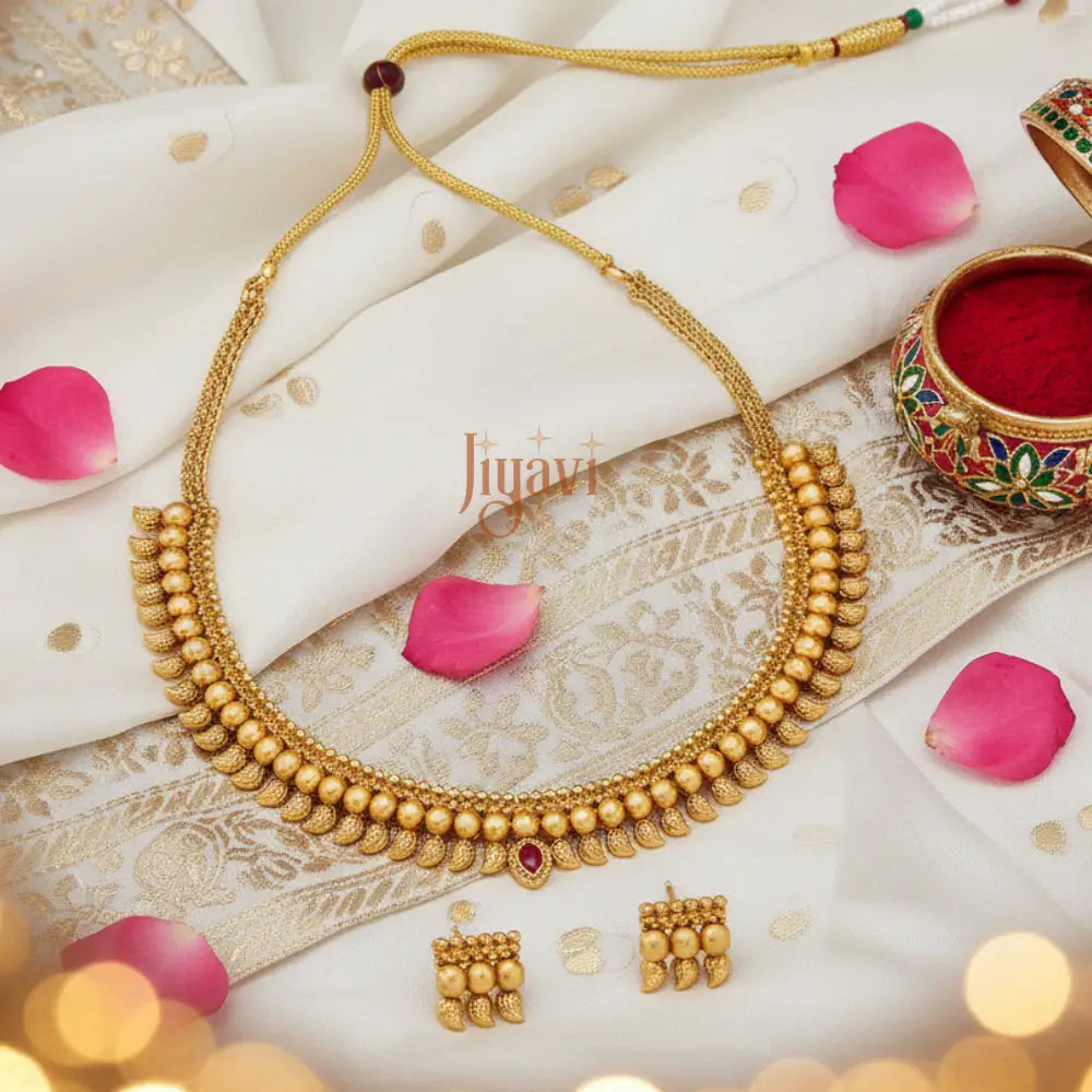 Gold necklace and earrings on a decorative fabric background with pink petals and a small bowl.