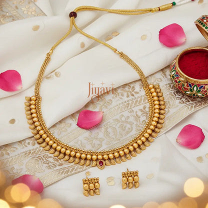 Gold necklace and earrings on a decorative fabric background with pink petals and a small bowl.