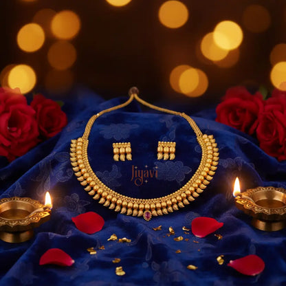 Gold necklace and earrings set on a blue fabric with red roses and Diwali lamps.
