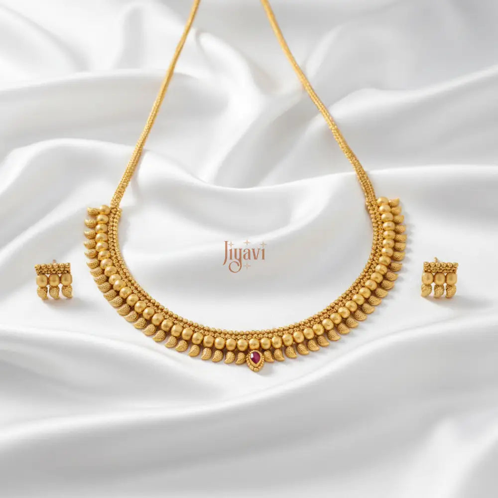 Gold necklace and earrings set on a white fabric background with 'Jiyavi' branding.