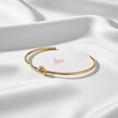 gold-plated, open cuff bangle bracelet with a knot design on white satin