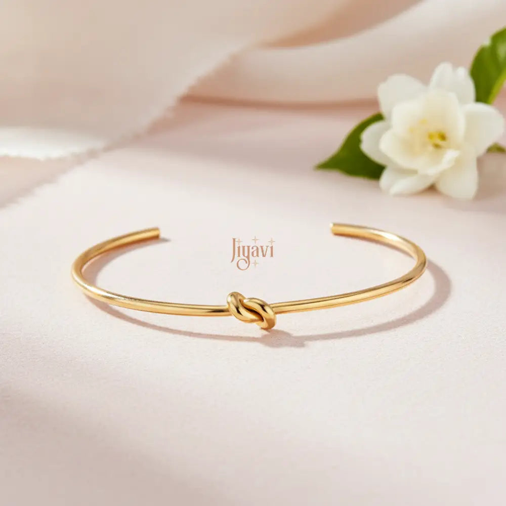 gold-plated, open cuff bangle bracelet with a knot design on peach color background