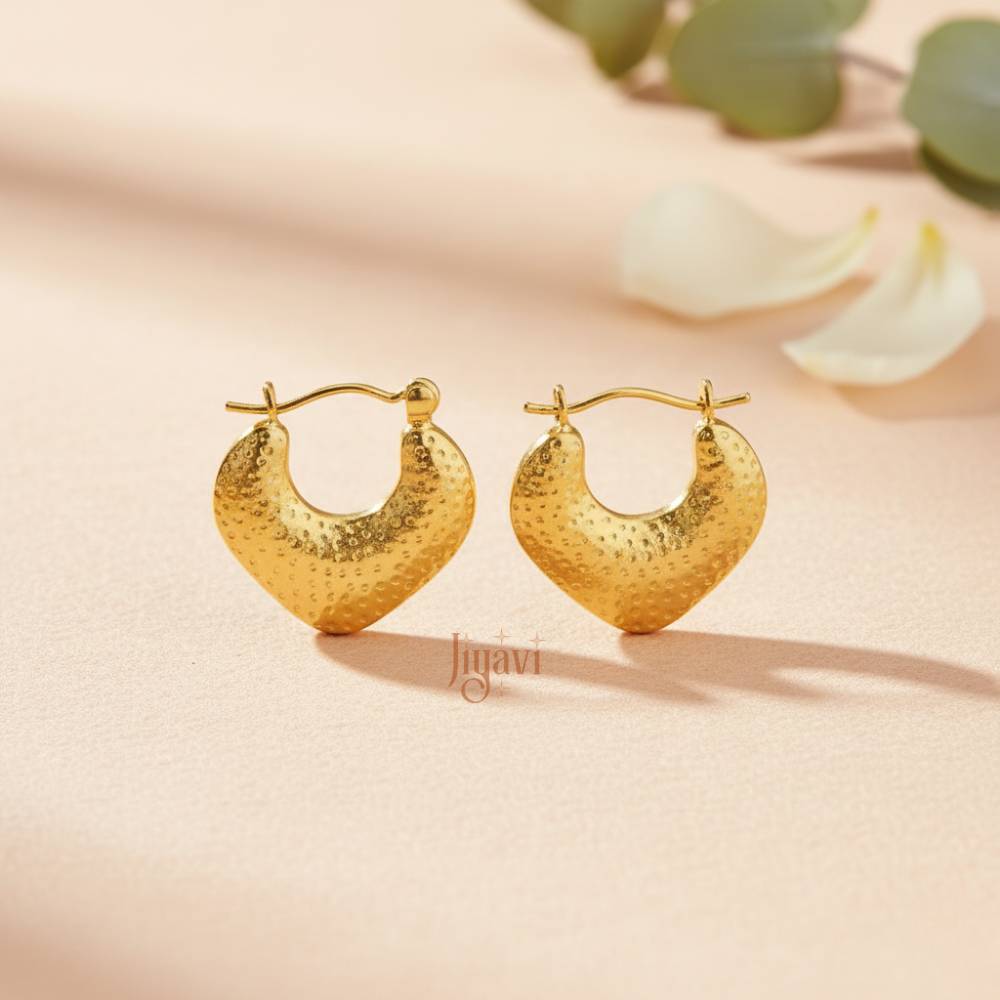 Gold hoop earrings on a soft beige background with floral elements.