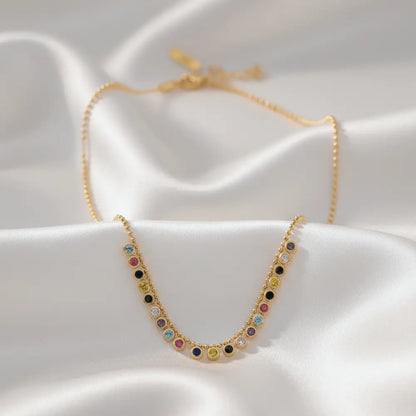 Gold plated necklace with colorful gemstones on a white fabric background