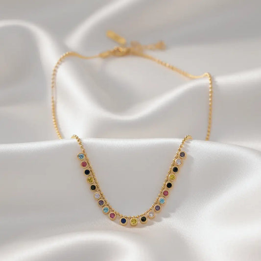 Gold plated necklace with colorful gemstones on a white fabric background