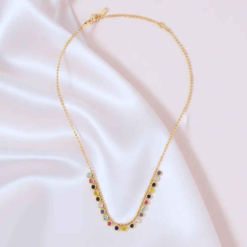 Gold plated necklace with colorful beads on a soft pink fabric background