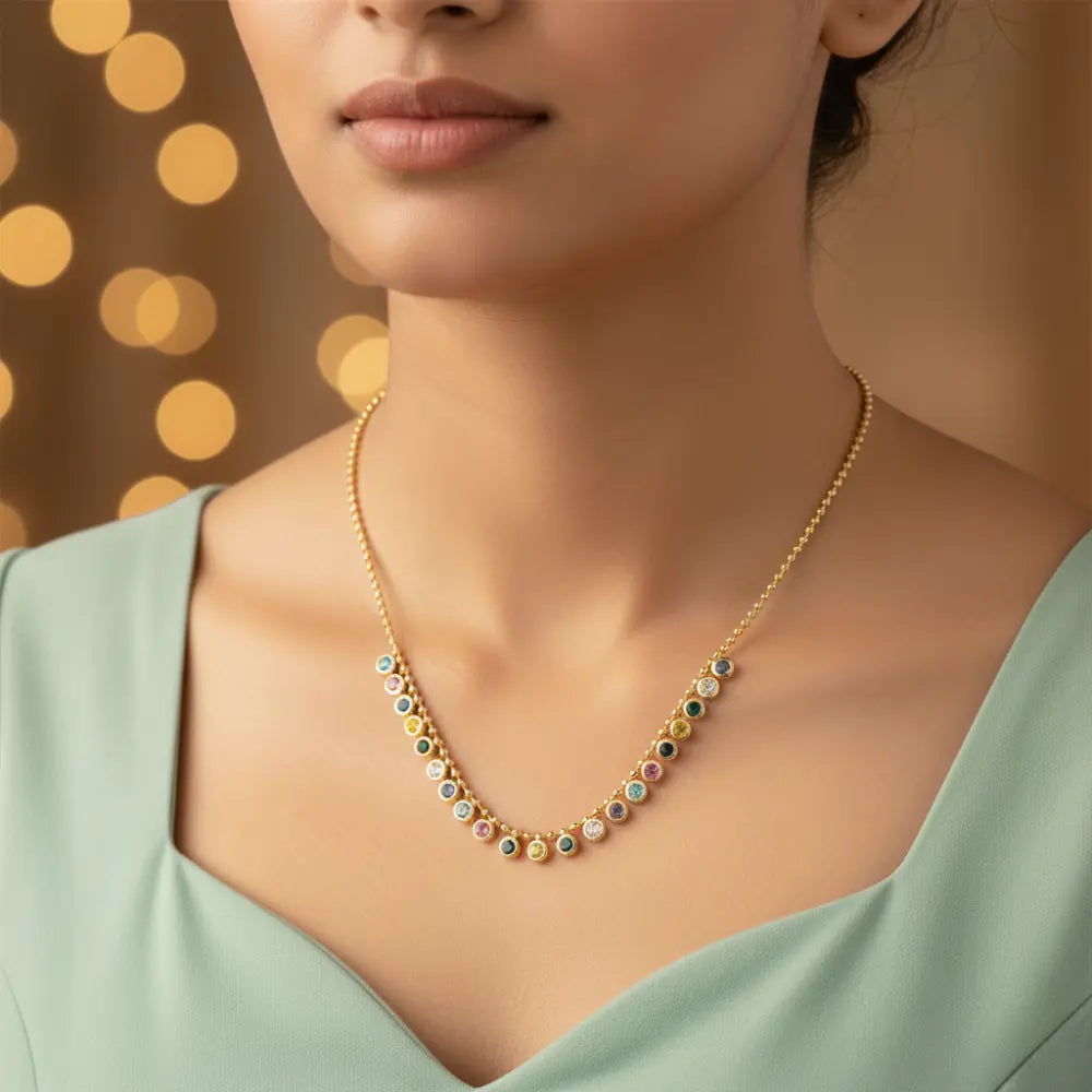 Gold plated necklace with multicolored stones worn by a model against a warm, blurred background
