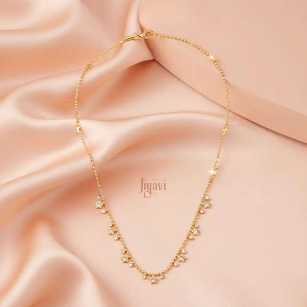 Gold necklace on a soft pink fabric with 'Jiguavi' branding.