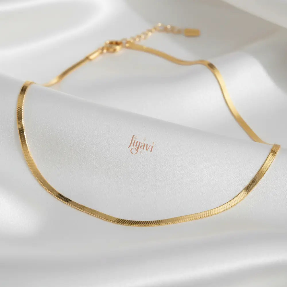 Gold necklace on a white fabric background with 'Jugavi' branding.