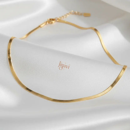Gold necklace on a white fabric background with 'Jugavi' branding.