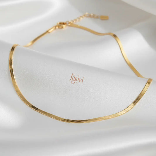 Gold necklace on a white fabric background with 'Jugavi' branding.
