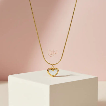 Gold necklace with a heart pendant on a white pedestal against a pink background