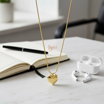 Gold necklace with a heart pendant on a table next to white earbuds and an open book.