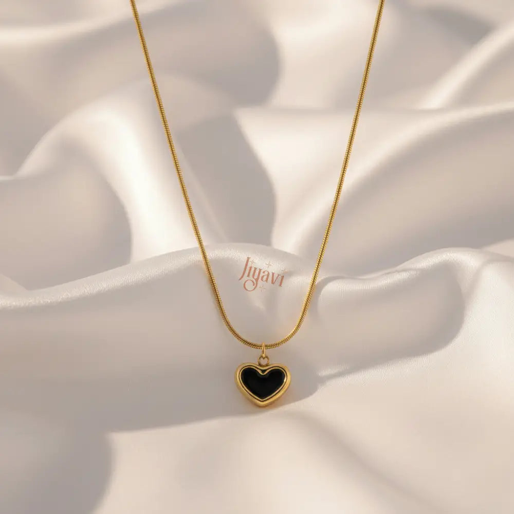 Gold necklace with a black heart pendant on a white fabric background