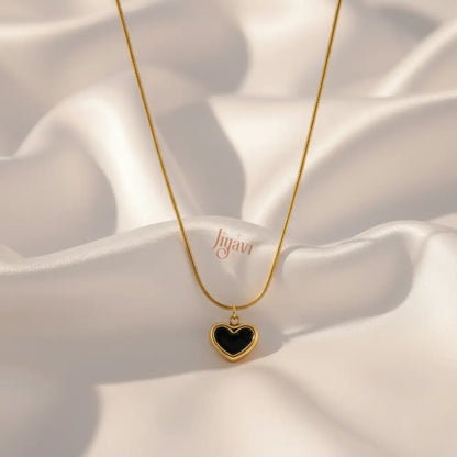 Gold necklace with a black heart pendant on a white fabric background