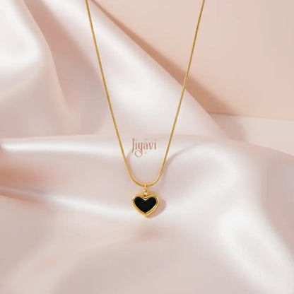 Gold necklace with a black heart pendant on a soft pink fabric background, featuring the brand 'Jiguavi'.