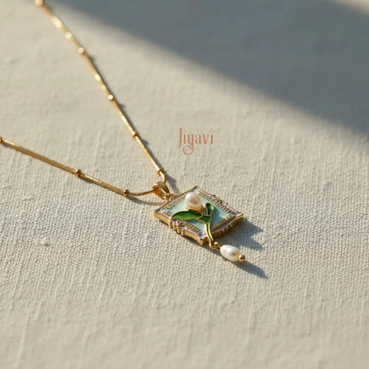 Delicate necklace with a pendant featuring a leaf and pearl on a textured surface, branded 'Jiyavi'.