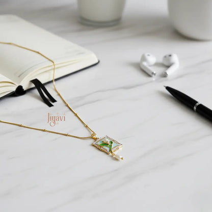 Gold necklace with a pendant on a white surface, next to an open book and a pen.