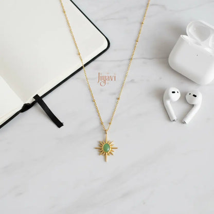 Gold necklace with a green pendant on a white surface next to a notebook and white earbuds.