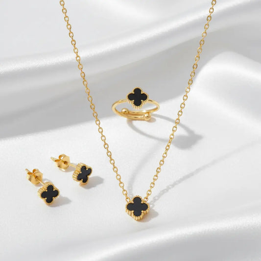 Gold jewelry set with black clover designs on a white surface