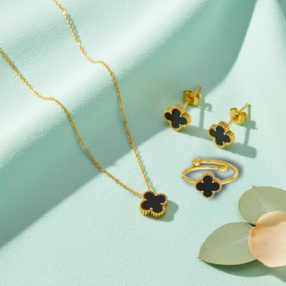Gold jewelry set with black clover designs on a light green background