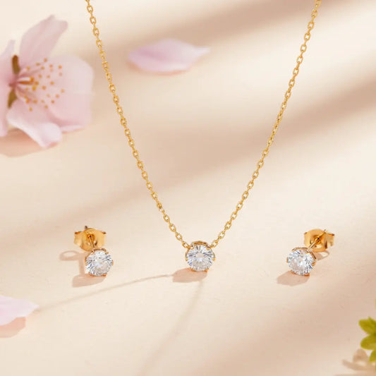 Gold necklace and earrings with diamond-like stones on a soft pink background