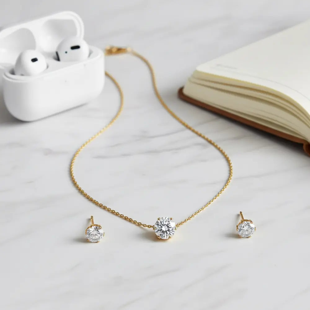 Gold necklace with diamond pendants and earrings on a light surface with an open book and white case.